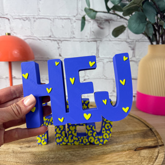 3D-Schriftzugs HEJ in Blau mit gelben Herzchen, in der Hand gehalten