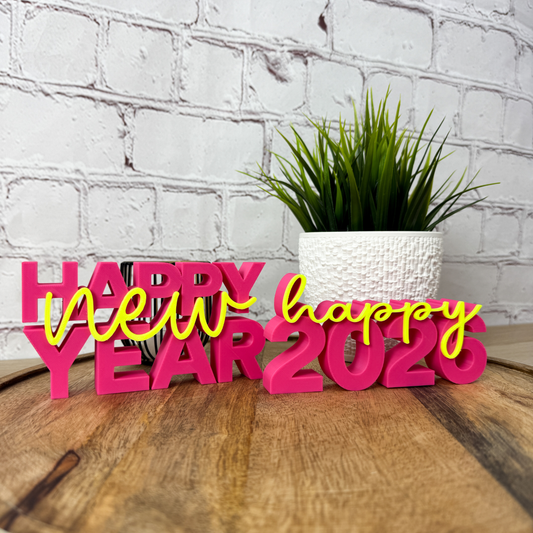 3D Schriftzug „happy new year“ und "happy 2026" aus PLA in Pink und Gelb als Silvester-Deko, auf Holztisch vor weißer Wand platziert