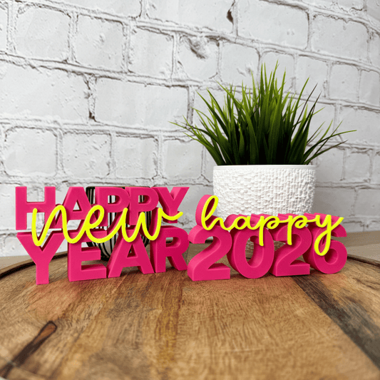 3D Schriftzug „happy new year“ und "happy 2026" aus PLA in Pink und Gelb als Silvester-Deko, auf Holztisch vor weißer Wand platziert