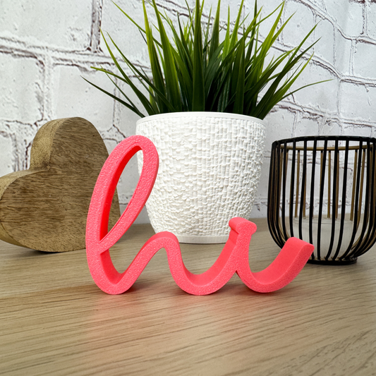 Rosa 3D-Schriftzug „hi“ aus PLA+ auf Holztisch, dekoriert mit Pflanze und Holzherz – ideale Deko zum Einzug oder Geburtstag