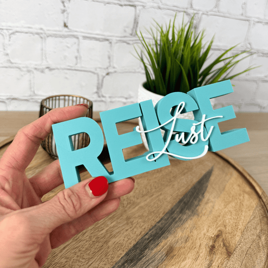 Türkiser 3D Schriftzug „REISE“ mit weißem Wort „Lust“, frontale Ansicht auf Holzuntergrund mit Pflanze