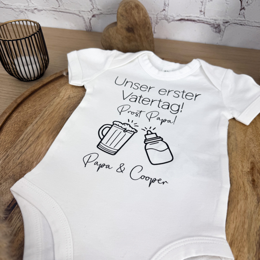 Kurzarm Body aus Bio Baumwolle und "Unser erster Vatertag – Prost Papa"-Design, eine süße Geschenkidee für den ersten Vatertag.