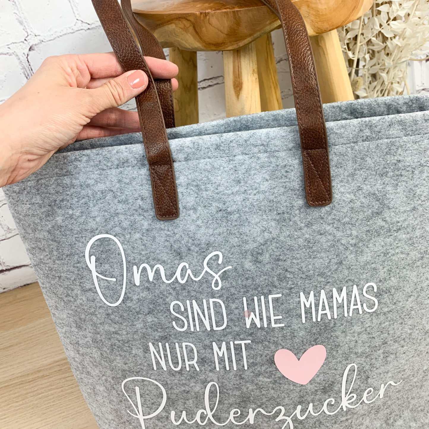 Detailaufnahme der hochwertigen Lederhenkel einer hellgrauen Filztasche mit personalisierbarer Aufschrift.