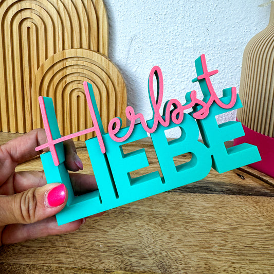 Herbst Liebe Schriftzug wird in der Hand gehalten, Holzdeko und Vase im Hintergrund.