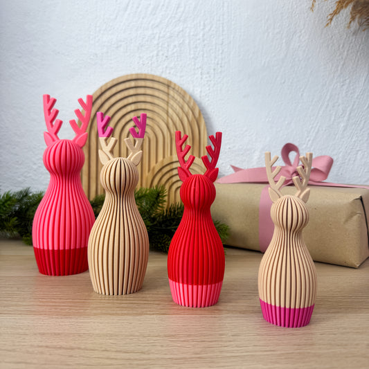 Vier Rentier Figuren mit individuell gewählten Farben vor einem Holzbogen und einem Geschenk mit rosa Schleife