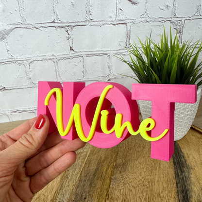 3D Schriftzug „Wine not“ aus PLA in Pink und Neon-Gelb, 15 cm breit, als dekoratives Geschenk für Geburtstag, gehalten in einer Hand