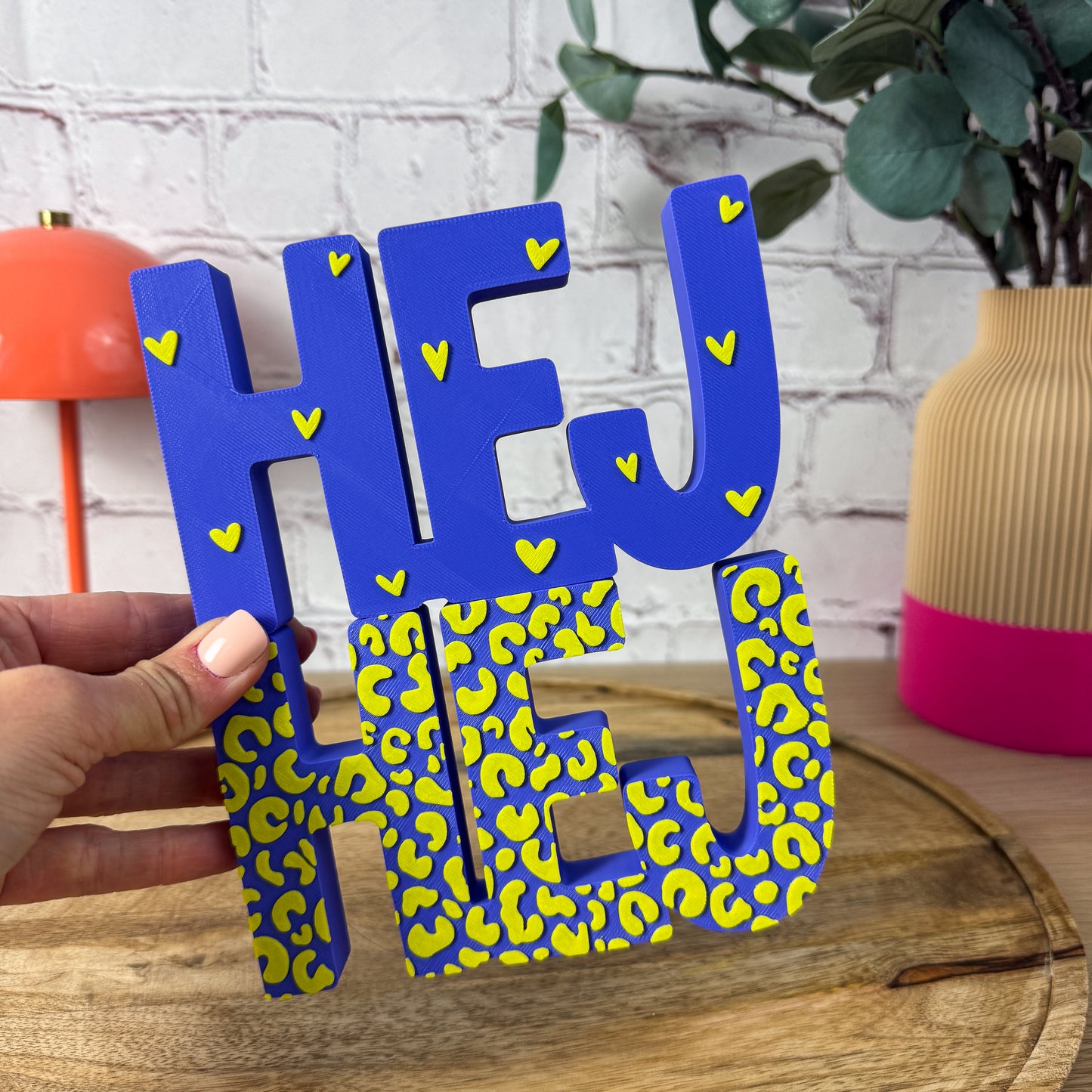 3D-Schriftzug HEJ in Blau mit gelbem Leopardenmuster und gelben Herzchen, in der Hand gehalten