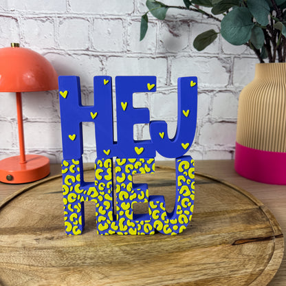3D-Schriftzug HEJ auf Holztablett, blau mit gelbem Leo-Muster und Herzchen