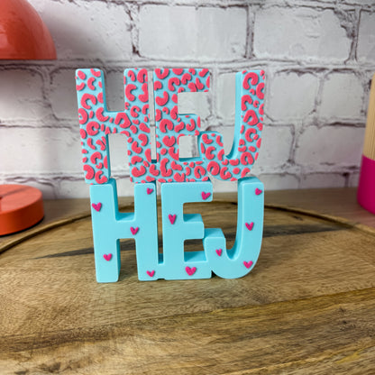 3D-Schriftzug HEJ in Türkis mit pinkem Leopardenmuster und pinken Herzchen auf Holztablett
