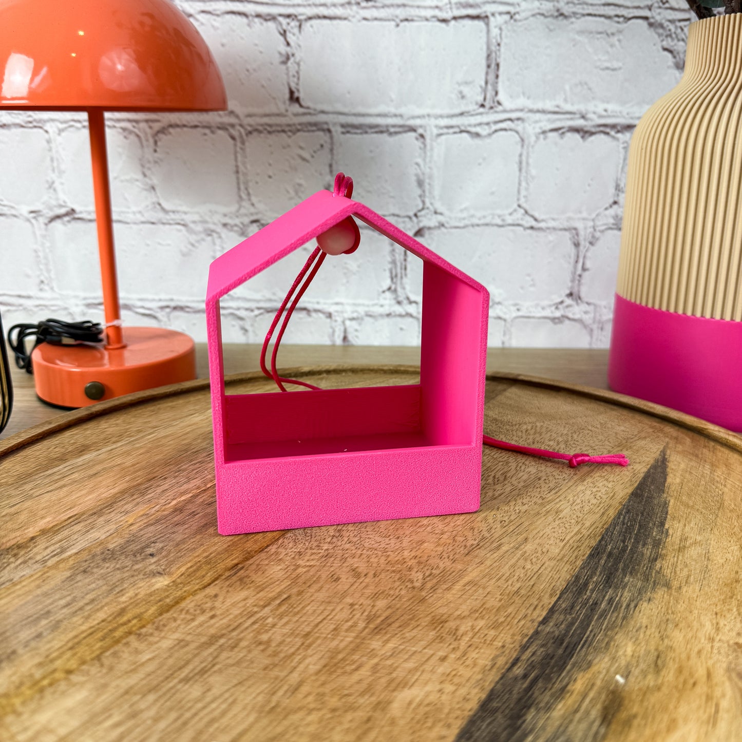 Einzelne 3D-gedruckte Vogelfutterstation in Pink mit pinkfarbenem Band und runder Holzperle