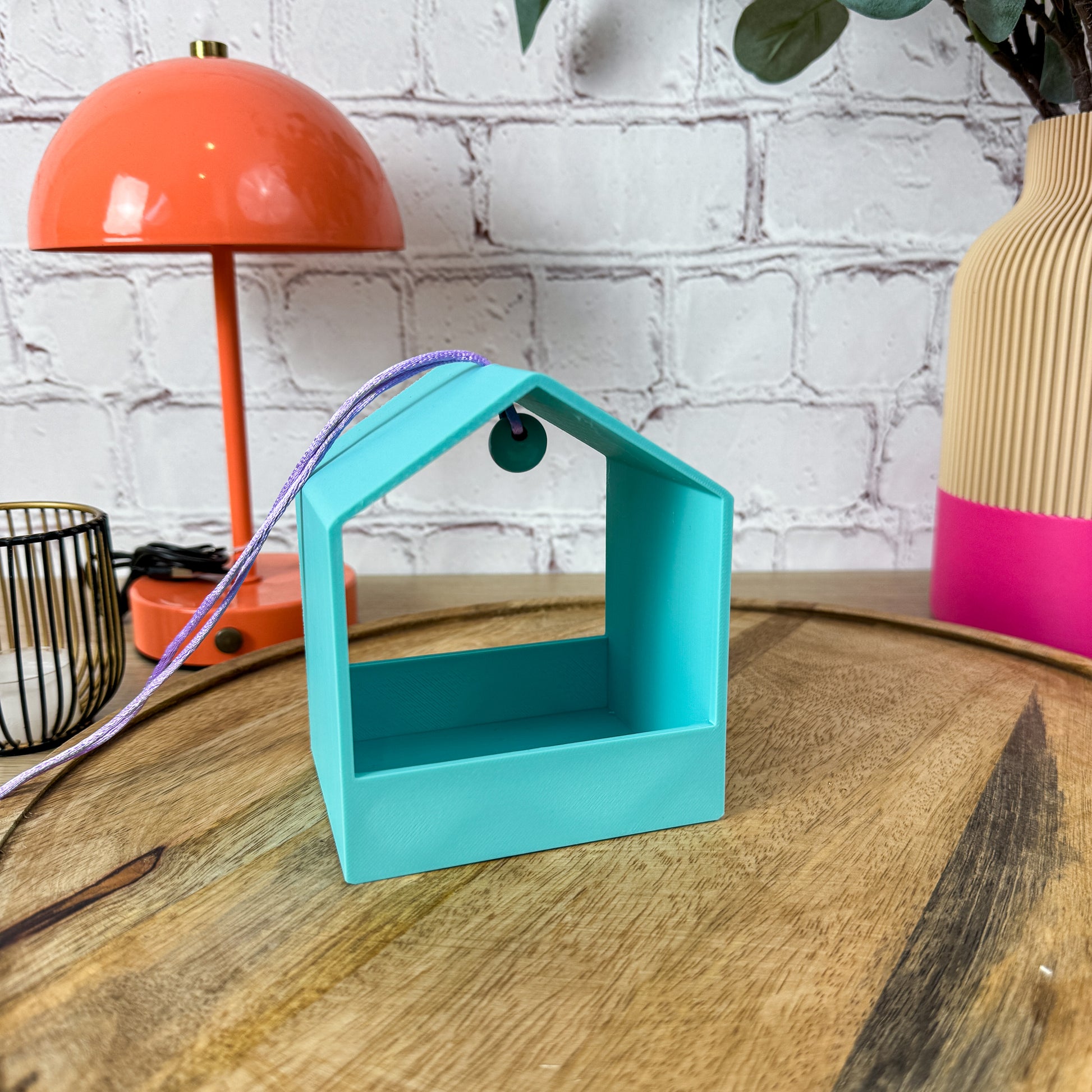 Einzelne 3D-gedruckte Vogelfutterstation in Türkis mit lila Band und grüner Holzperle