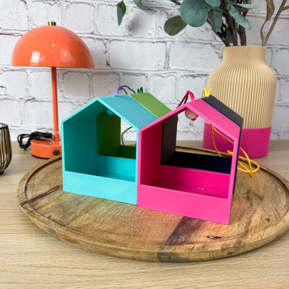 Vier 3D-gedruckte Vogelfutterstationen zum Hängen in Türkis, Grün, Pink und Dunkelblau auf Holztablett