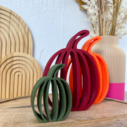3D gedruckter Kürbis flach in drei Farben auf einem Holzbrett vor Holzbögen und Deko-Vase