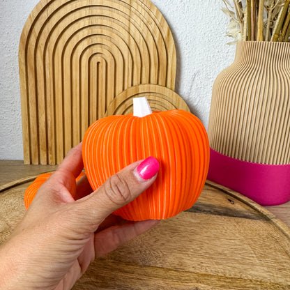 Großer 3D Kürbis Skandi in Orange in einer Hand gehalten, Größenvergleich vor Holzbögen und Vase