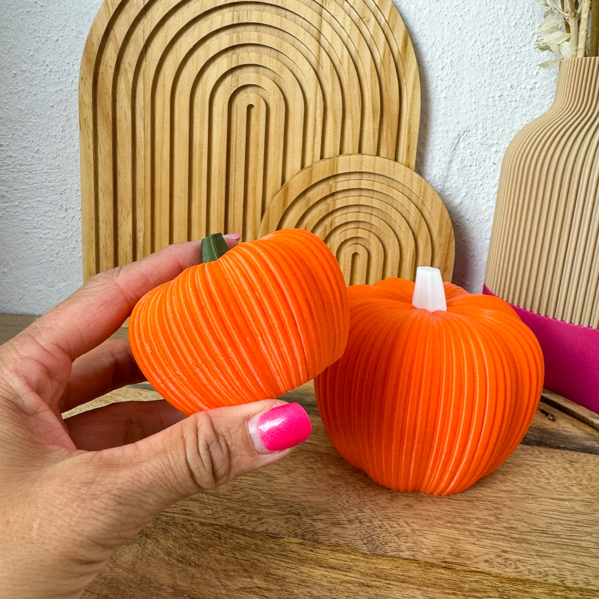 Kleiner 3D Kürbis Skandi in Orange in einer Hand gehalten, große Variante daneben als Größenvergleich