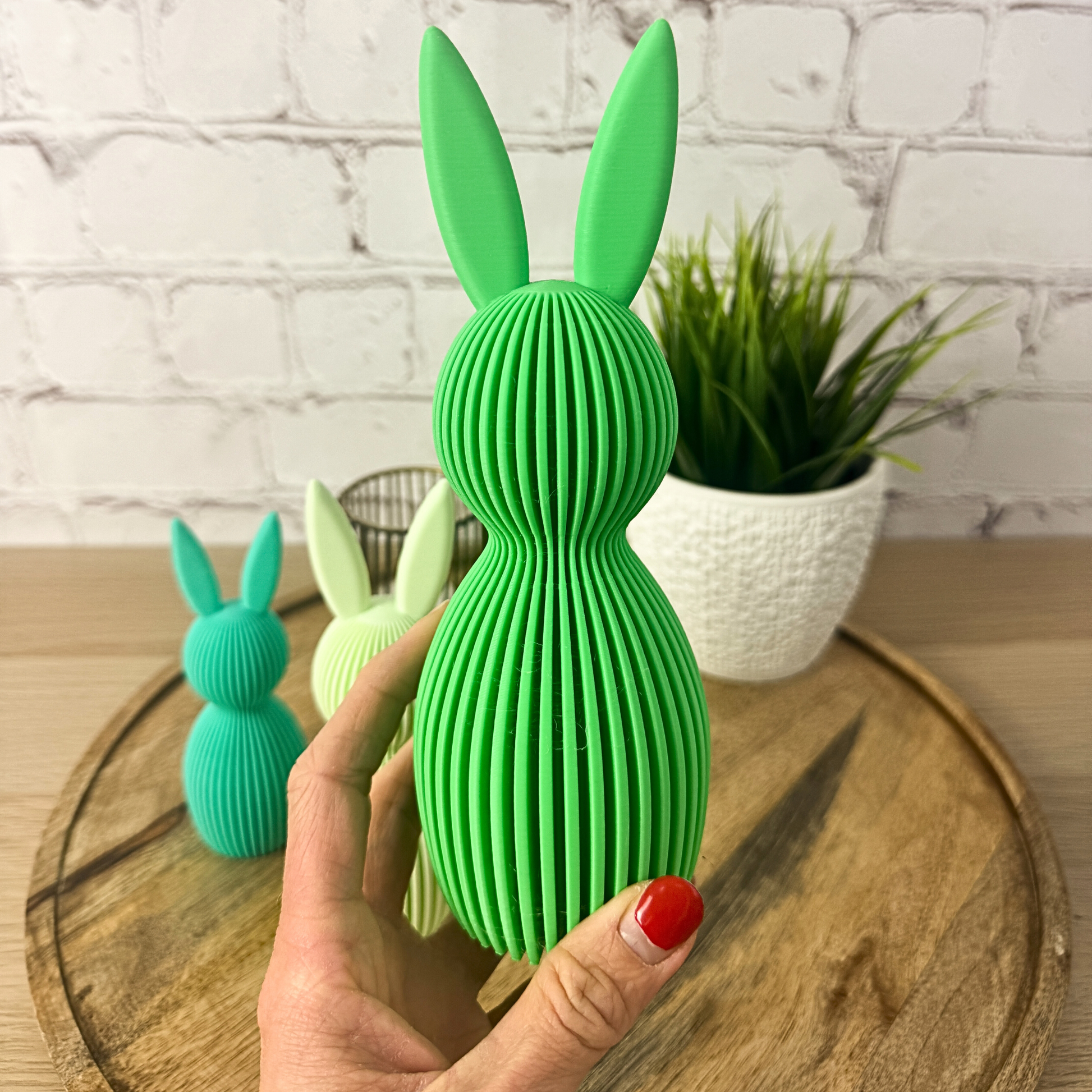 Geriffelter 3D Osterhase aus PLA in kräftigem Grün, in der Hand gehalten auf Holztablett vor Ziegelwand