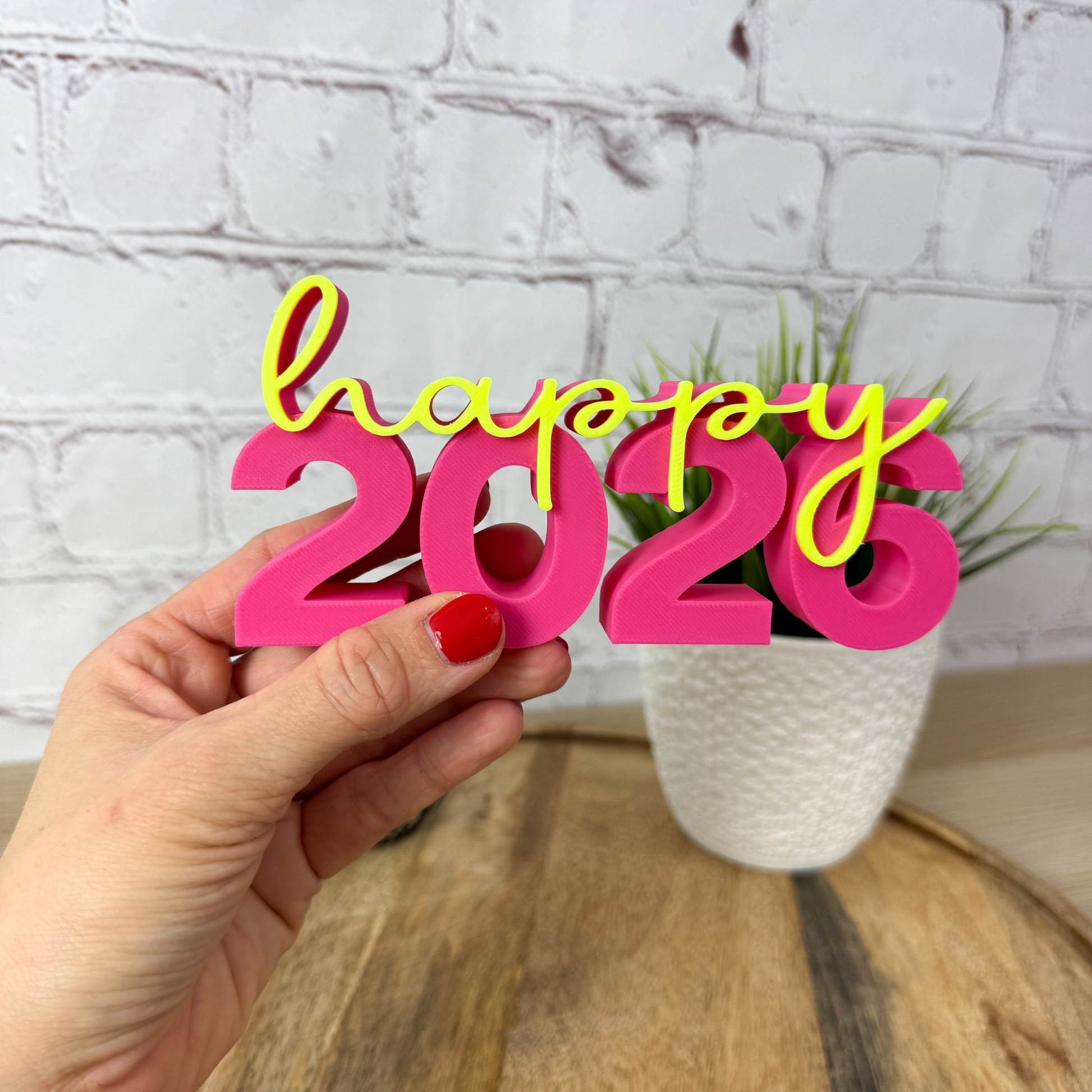 3D Schriftzug „happy 2026“ in pink-gelb, in der Hand gehalten, kleine Silvester-Tischdeko aus PLA