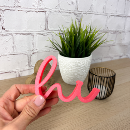Hand hält rosa 3D-Schriftzug „hi“ aus PLA+ vor Pflanze und Deko – perfekte Geschenkidee für Einzug oder Geburtstag