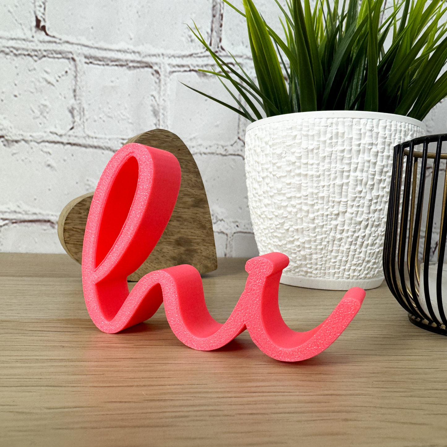 Rosa 3D-Schriftzug „hi“ aus PLA, dekorativ vor Pflanze und Holzherz arrangiert – moderne Tischdeko