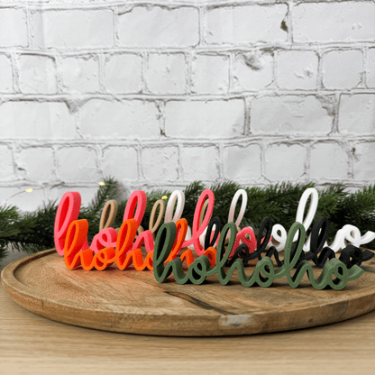 Mehrere hohoho 3D-Schriftzüge in Rosa, Orange, Dunkelgrün, Weiß, Beige und Schwarz nebeneinander