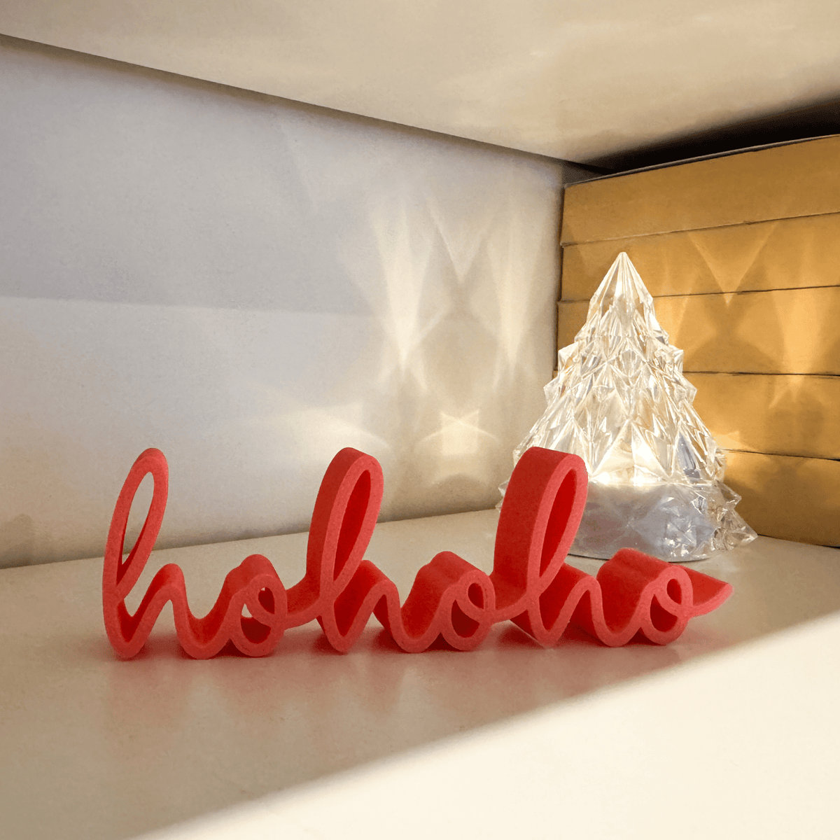 hohoho 3D-Schriftzug in Rosa auf einem Regal, daneben ein beleuchteter Weihnachtsbaum aus Kristallglas