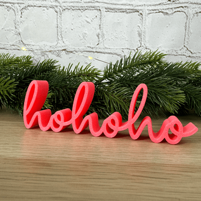 hohoho Schriftzug in Rosa vor Tannenzweigen und Lichterkette, aufgestellt auf einer Holzfläche