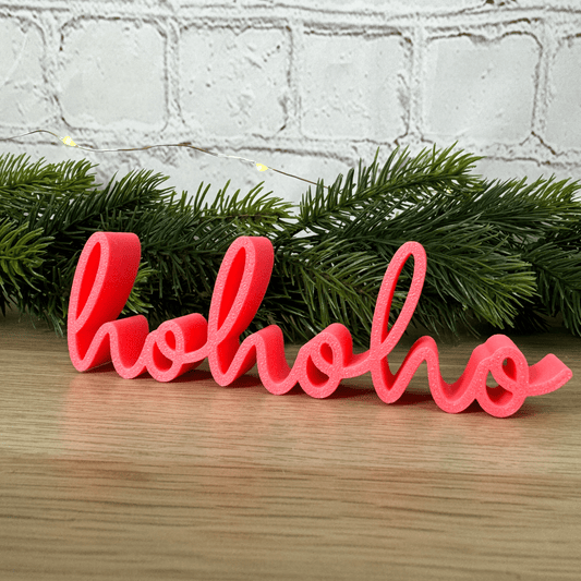 hohoho Schriftzug in Rosa vor Tannenzweigen und Lichterkette, aufgestellt auf einer Holzfläche