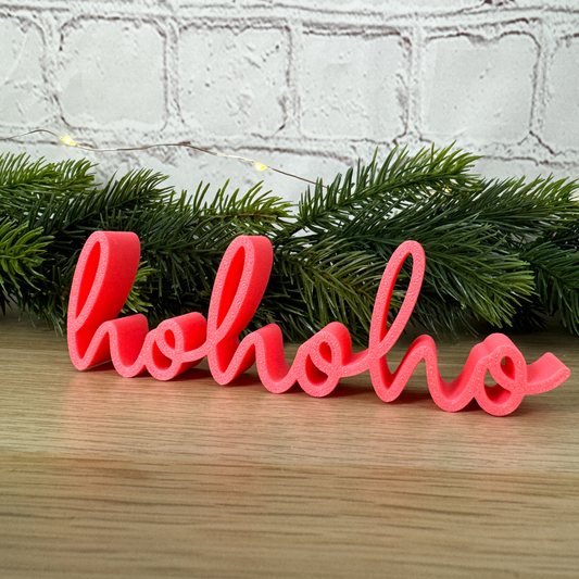 3D Schriftzug „hohoho“ aus PLA in Rosa, dekorativ gehalten vor grünem Tannenzweig – Weihnachtsdeko für Zuhause