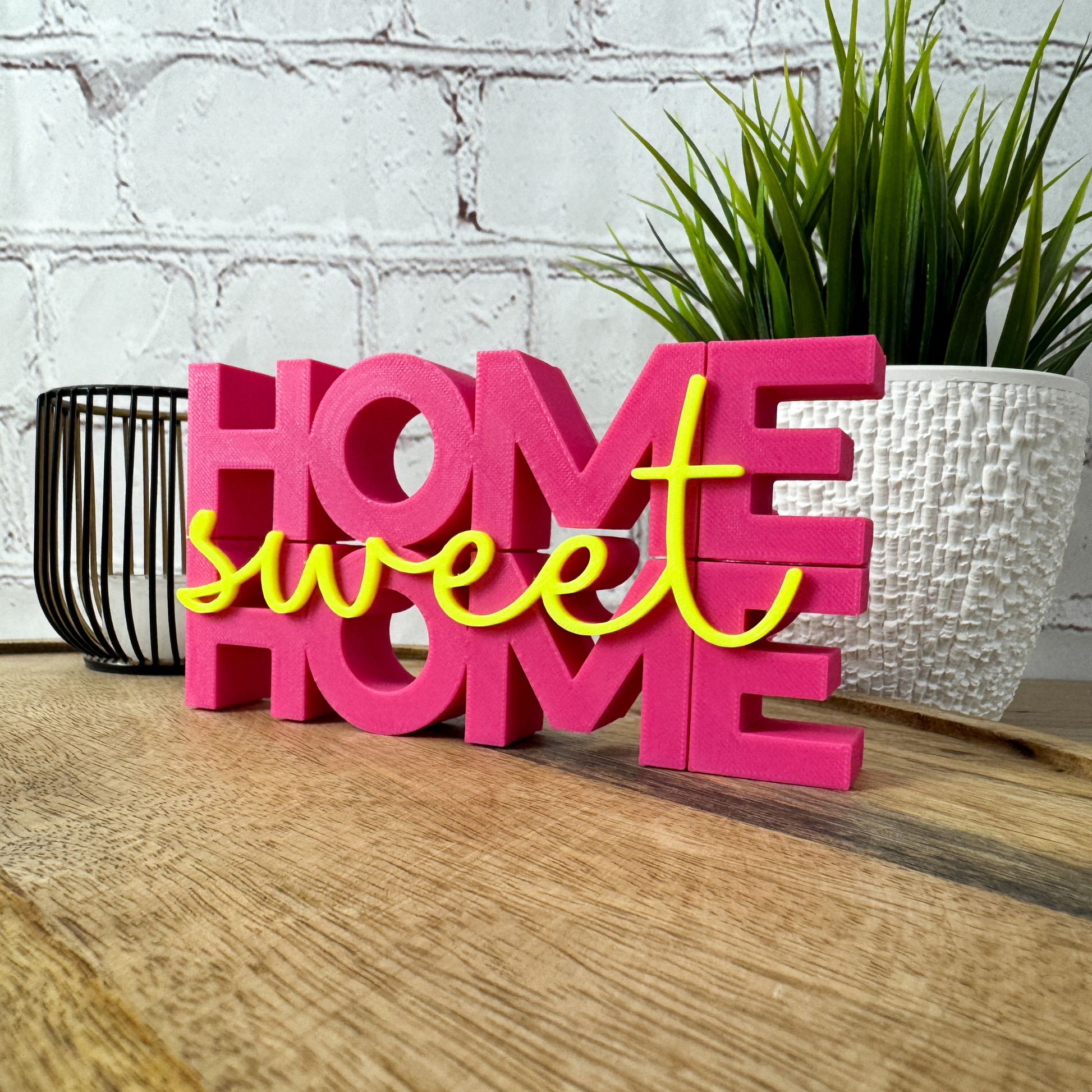PLA 3D Schriftzug „home sweet home“ in Magenta-Gelb, dekorativ auf Holztisch vor Pflanze als Einzugsdeko