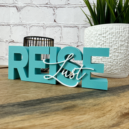 3D Schriftzug „REISE“ aus PLA in Türkis mit weißem Wort „Lust“, in der Hand gehalten auf Holzfläche
