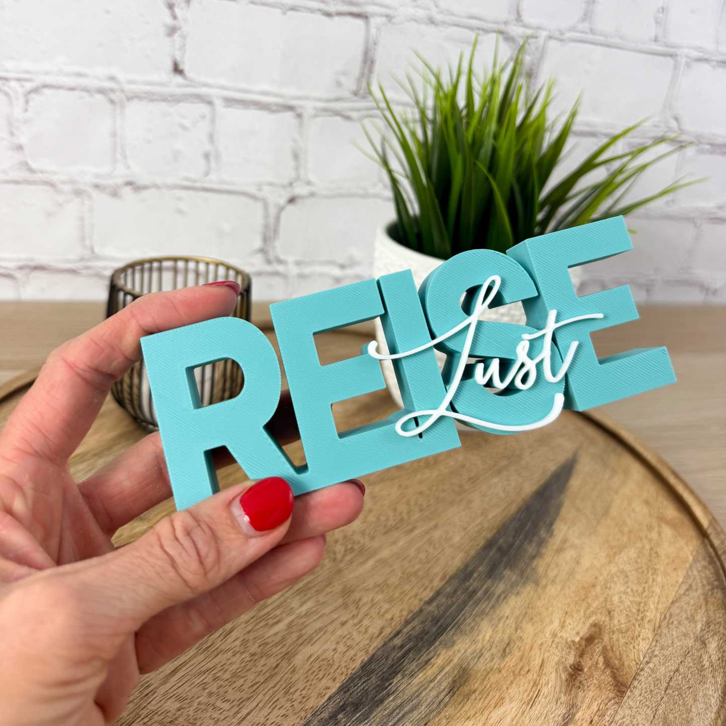 Türkiser 3D Schriftzug „REISE“ mit weißem Wort „Lust“, frontale Ansicht auf Holzuntergrund mit Pflanze