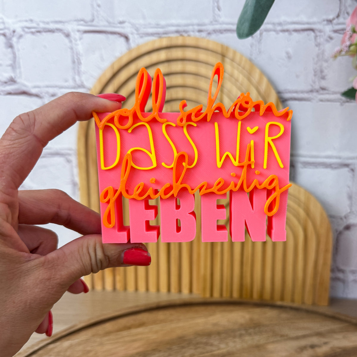 3D Spruch „Voll schön, dass wir gleichzeitig leben“ in Rosa, Gelb und Orange, Nahaufnahme in der Hand