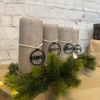 Vier graue Adventskerzen mit schwarzen PLA-Zahlenanhängern „eins“, „zwei“, „drei“, „vier“ – moderne Deko für den Adventskranz