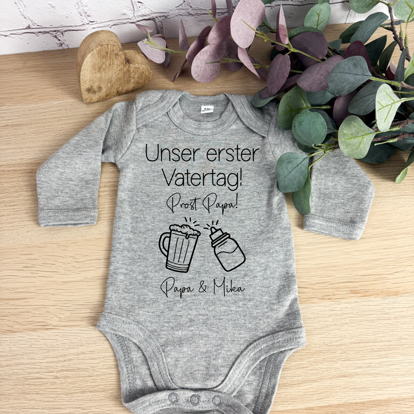 Grauer Babybody mit langen Ärmeln und "Unser erster Vatertag – Prost Papa"-Design, eine süße Geschenkidee für den ersten Vatertag.