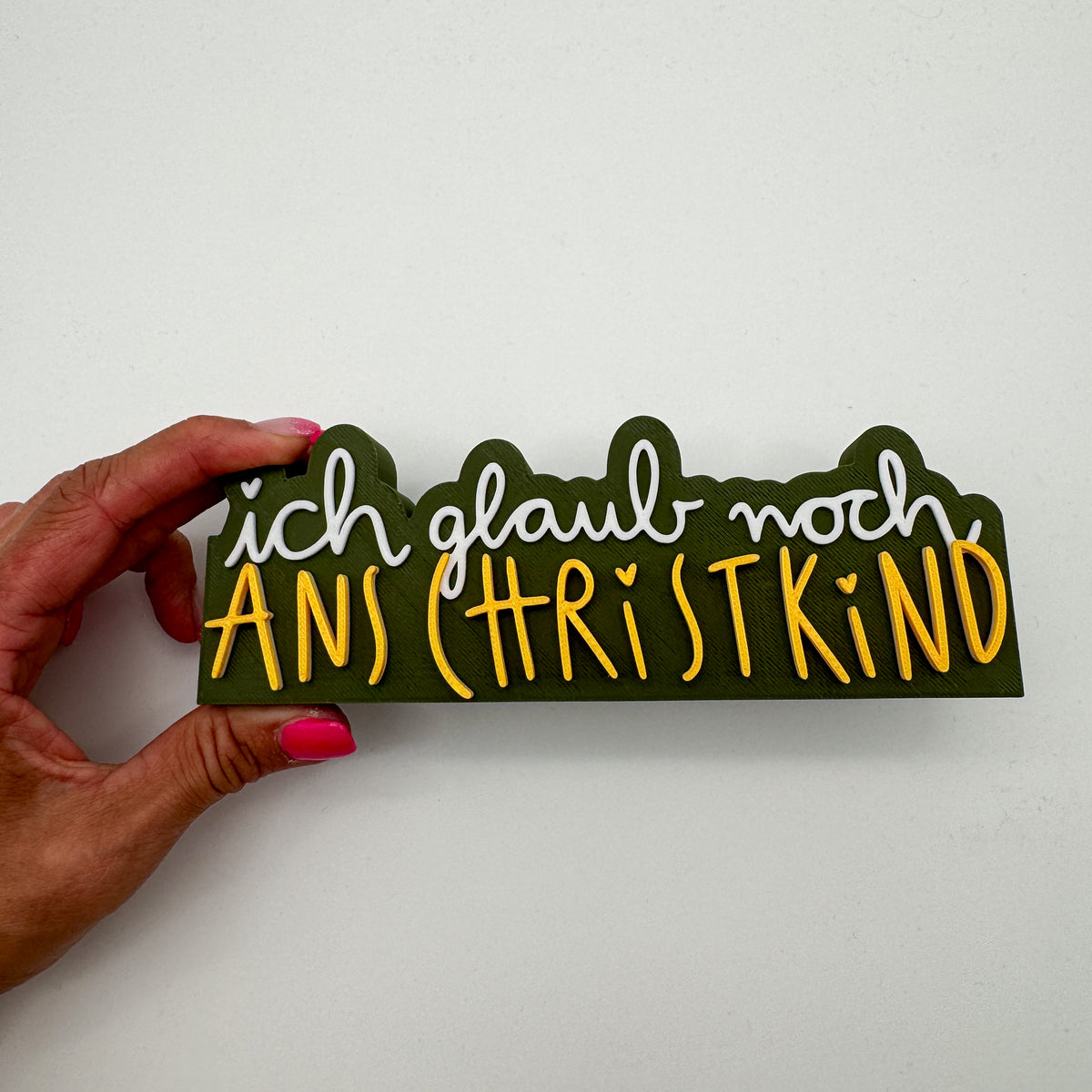Christkind-Spruch-Schild in Dunkelgrün, Weiß und Gold in einer Hand gehalten als Größenvergleich