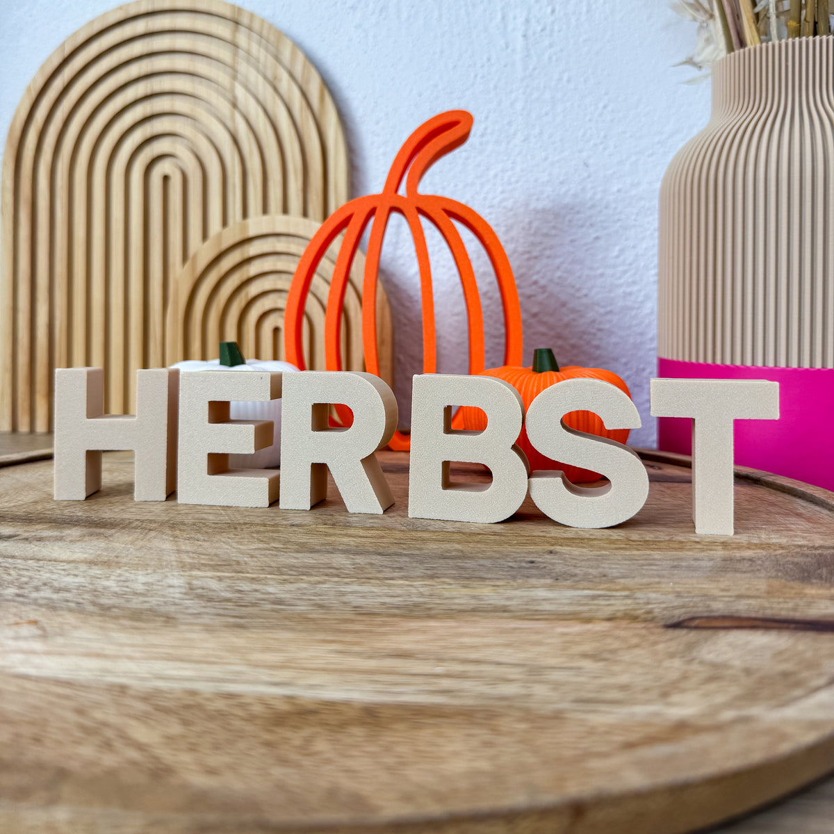 3D Buchstaben HERBST in Beige als Herbstdeko neben einem orangefarbenen Deko-Kürbis auf Holz