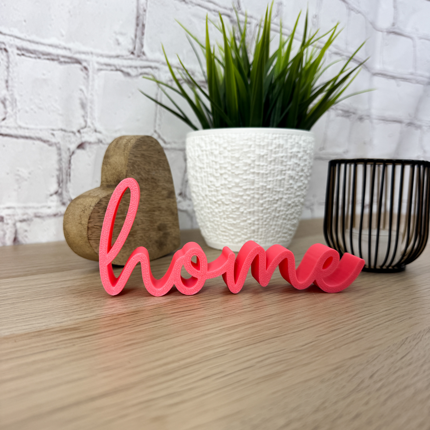 Dekorativer Schriftzug 'home' in Pink aus PLA+ vor einem weißen Blumentopf und Holzherz – ideales Geschenk zum Einzug.