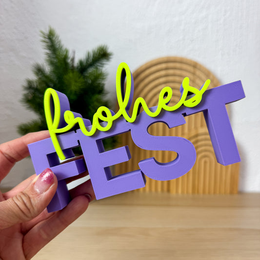 3D Schriftzug „frohes Fest” in Lila und Neongelb in einer Hand gehalten