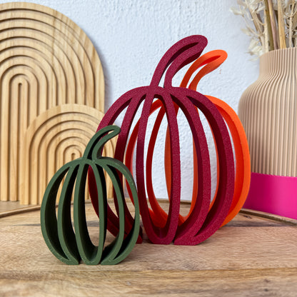 Herbstdeko Kürbis flach in Grün, Bordeaux und Orange nebeneinander auf Holz vor Vase und Trockenblumen