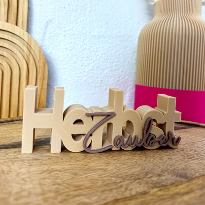 Herbstzauber Schriftzug als 3D Tischdeko in Beige und Braun vor Vase und Holzdeko.