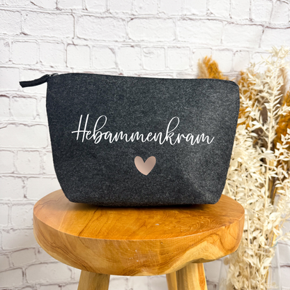 Dunkelgraue Kosmetiktasche aus Filz mit der Aufschrift „Hebammenkram“ und Herzmotiv – das perfekte Abschiedsgeschenk für Hebammen.