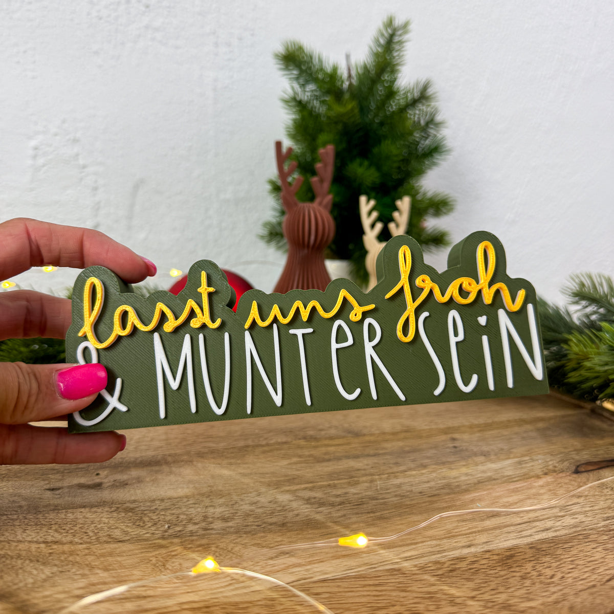 Schild „Lasst uns froh und munter sein" in Gold und Weiß in einer Hand gehalten als Größenvergleich