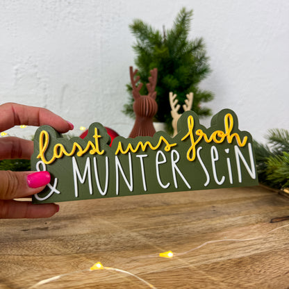 Schild „Lasst uns froh und munter sein" in Gold und Weiß in einer Hand gehalten als Größenvergleich