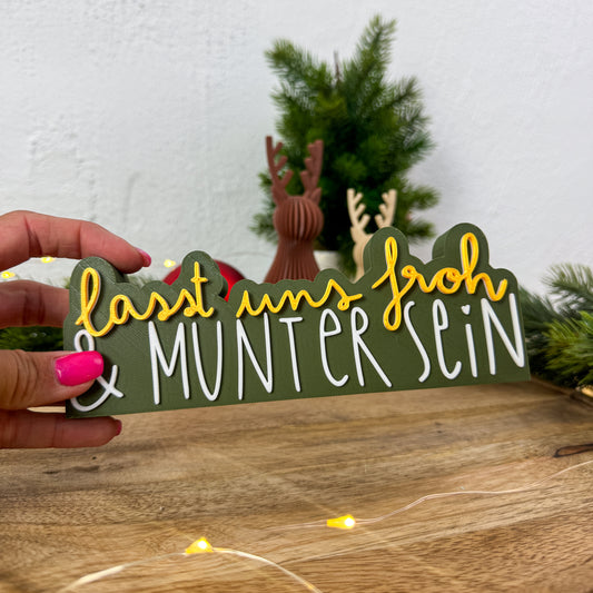 Schild „Lasst uns froh und munter sein" in Gold und Weiß in einer Hand gehalten als Größenvergleich