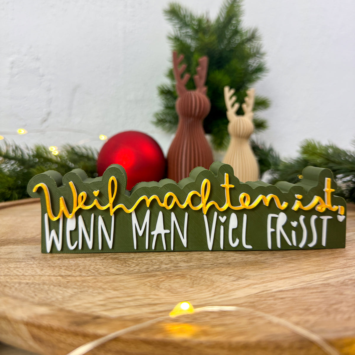 Lustiger Weihnachtsspruch „Weihnachten ist, wenn man viel frisst" in Nahaufnahme auf Holztisch