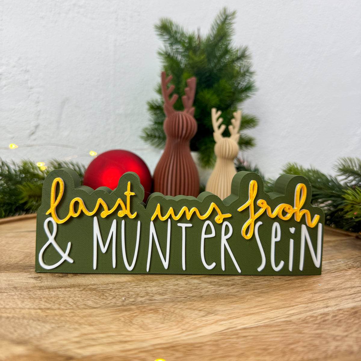 Nikolaus-Deko-Spruch „Lasst uns froh und munter sein" neben roter Christbaumkugel und Rentierfiguren