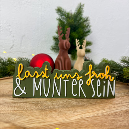 Nikolaus-Deko-Spruch „Lasst uns froh und munter sein" neben roter Christbaumkugel und Rentierfiguren