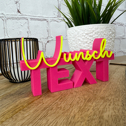 Personalisierter 3D-Schriftzug "Wunschtext" in magenta (pink) und Neongelb, seitliche Perspektive auf Holzuntergrund mit Pflanze