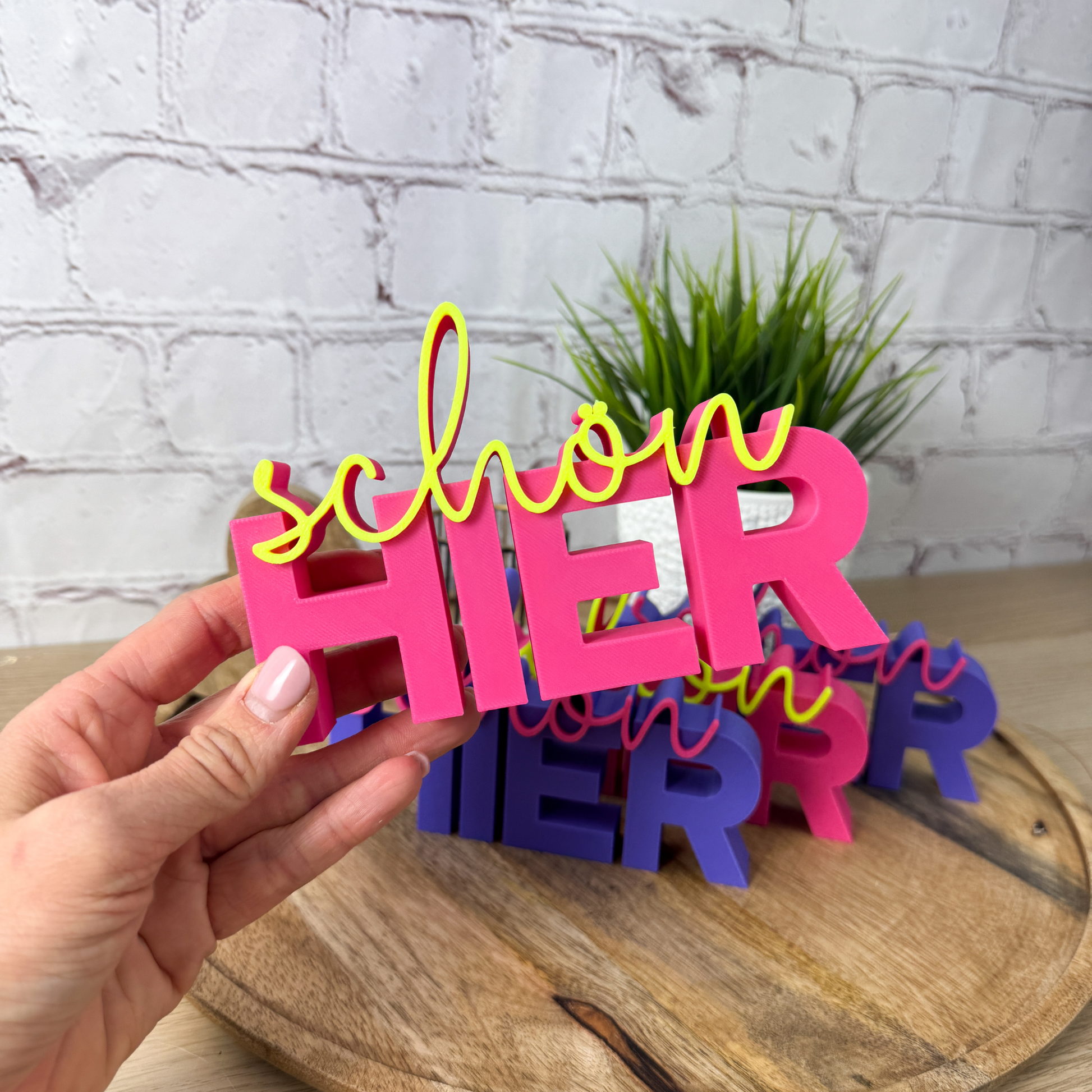 Schriftzug „schön hier“ in magenat-neon gelb, gehalten in Hand – liebevolle Geschenkidee mit Botschaft
