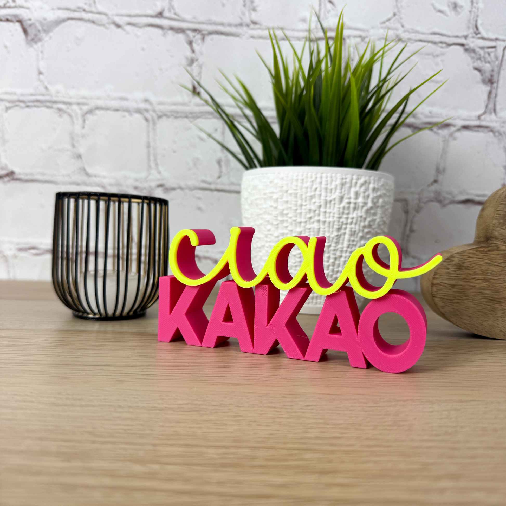 Bunter 3D-Schriftzug 'ciao kakao' in leuchtendem Pink und Gelb auf Holzuntergrund mit Dekoelementen